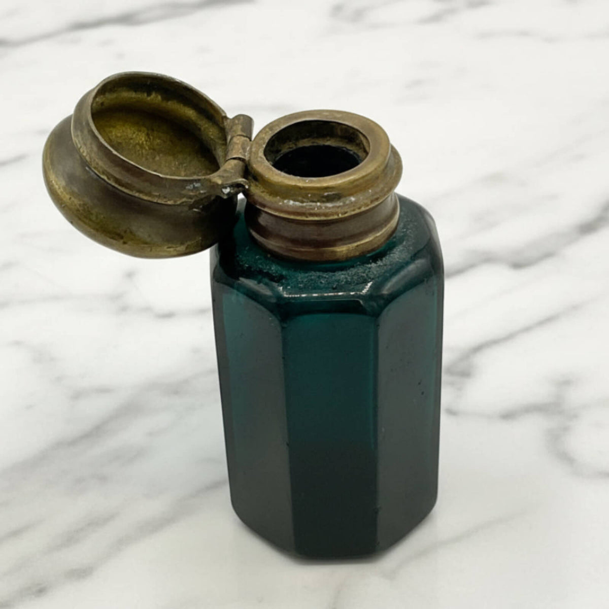 small blue bottle with an open lid on a marble surface