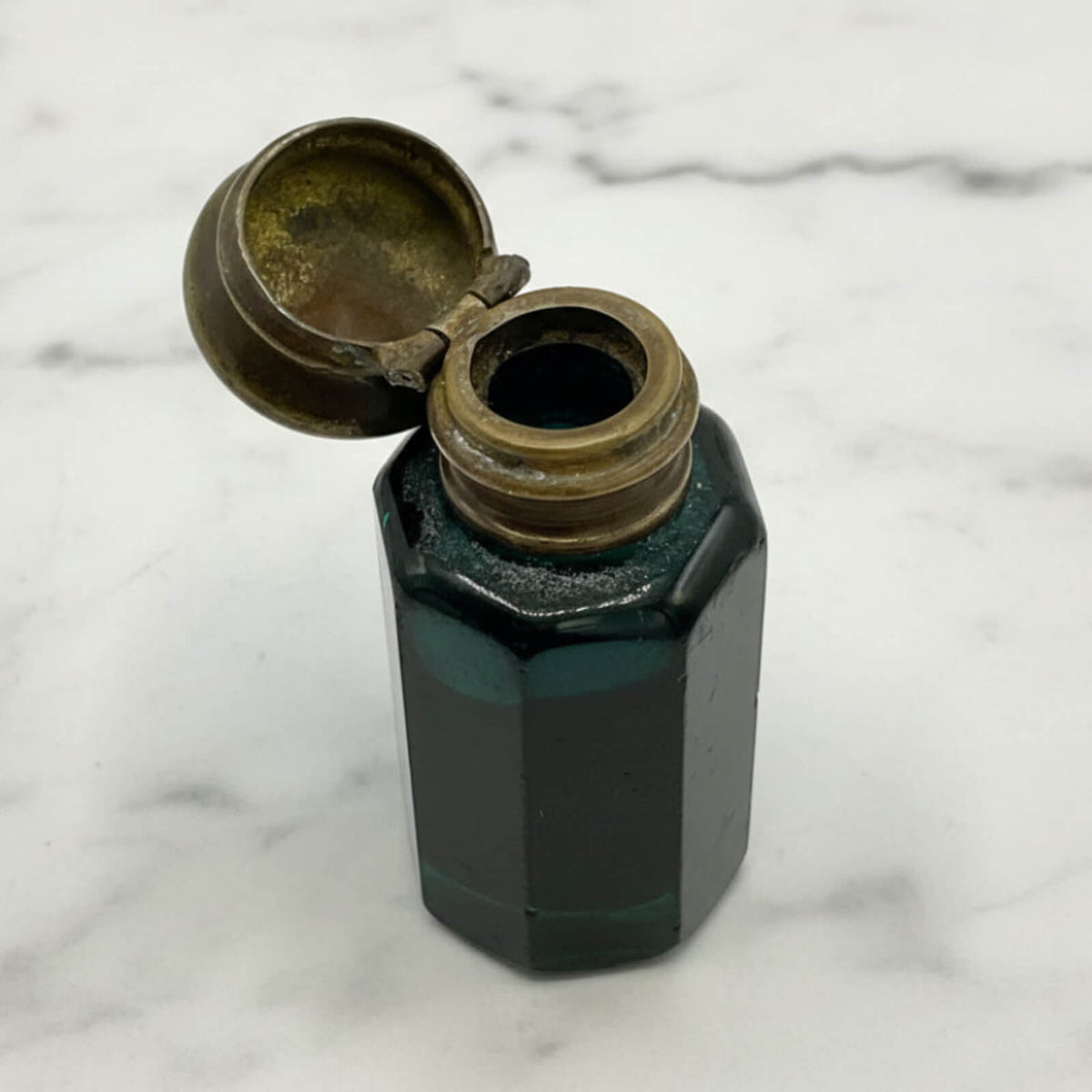 antique blue glass bottle with brass cap on a marble surface