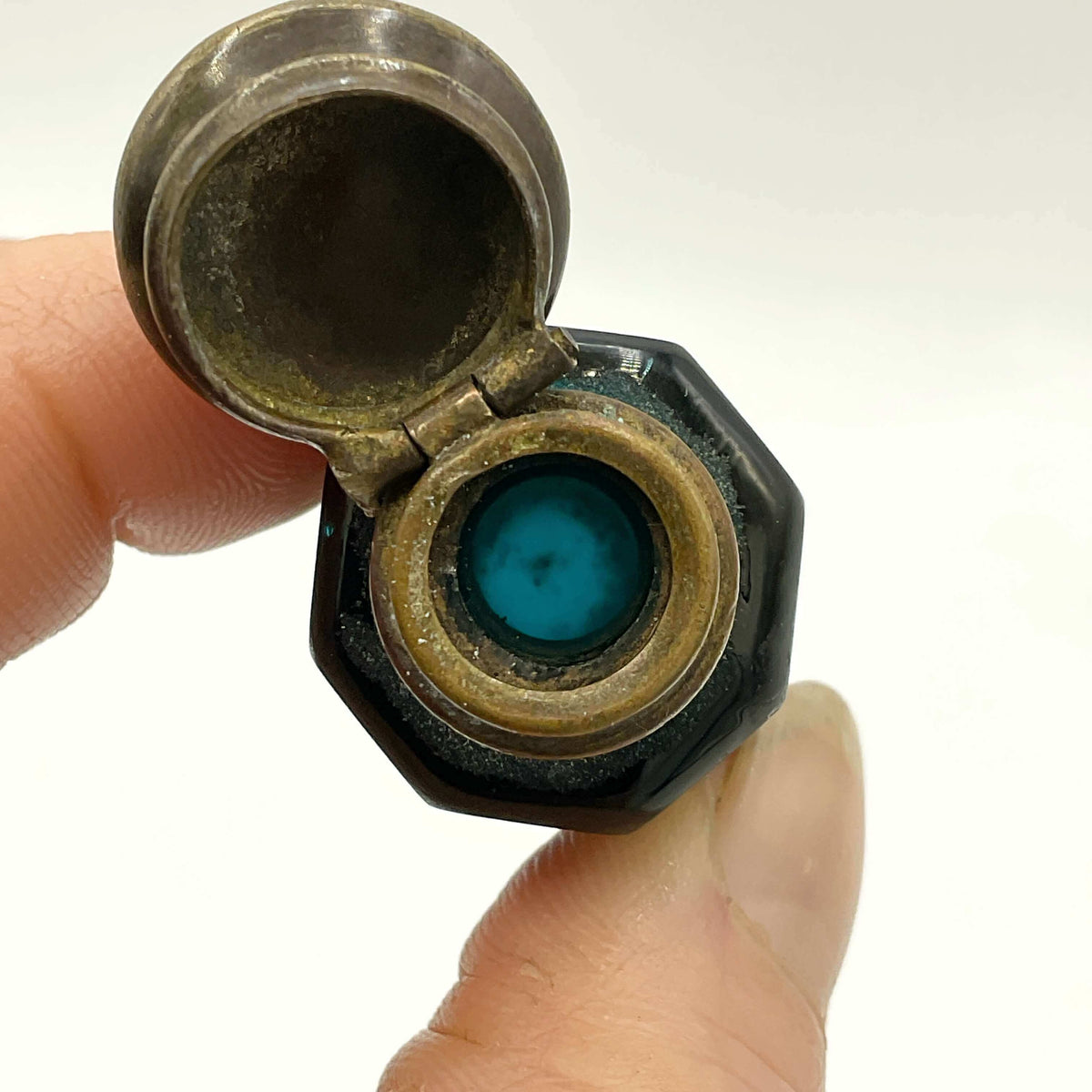 Close-up of a small glass bottle held between fingers against a white background