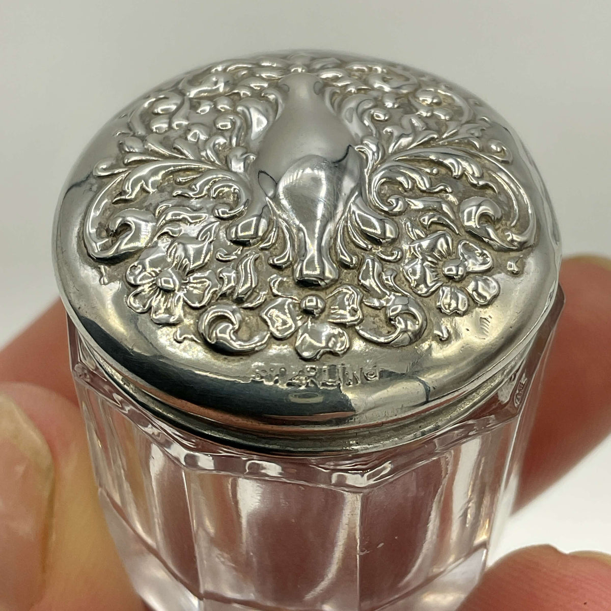 Decorative glass jar with a silver lid featuring intricate patterns.