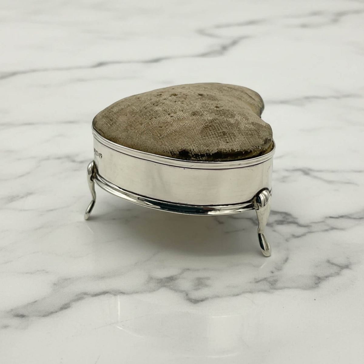 Silver pincushion with a textured lid on a marble surface