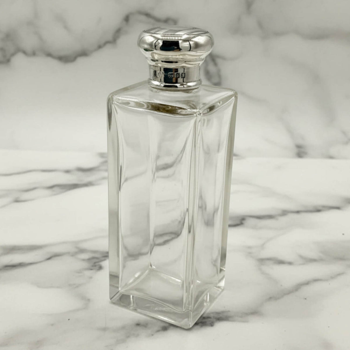 Clear glass bottle with silver cap on a marble background