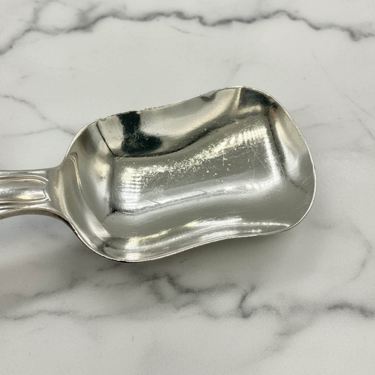 Antique Victorian Sterling Silver Spoon with a reflective, polished finish, resting on a white and gray marble surface.