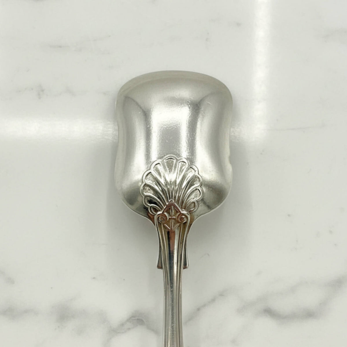 Antique Victorian Sterling Silver Spoon with an ornate shell pattern on the back of the bowl, resting on a white marble surface.