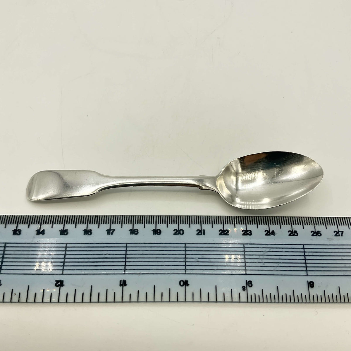 Antique Victorian Sterling Silver Teaspoon next to a ruler for scale on a white surface