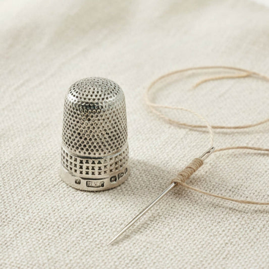Silver thimble and needle with thread on a textured fabric background