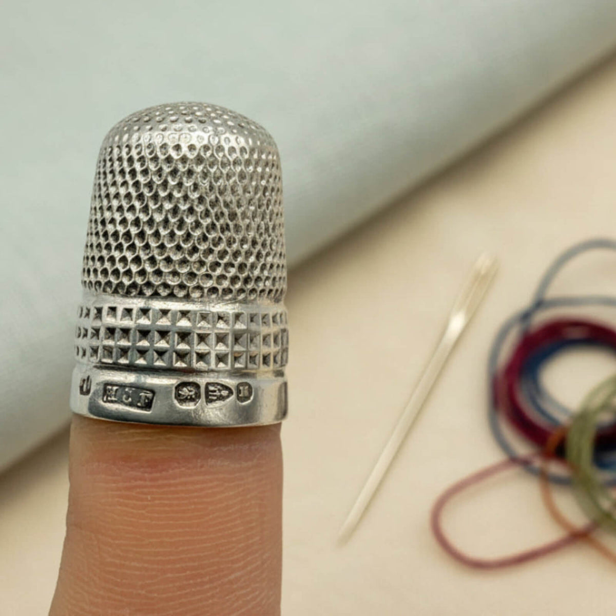 Silver thimble on a finger with sewing materials in the background