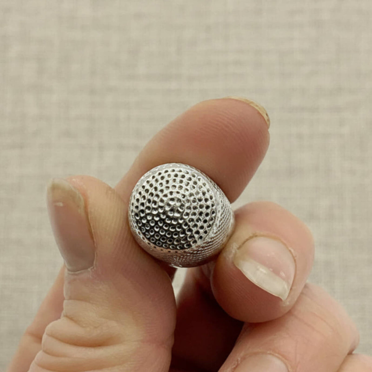 Silver textured thimble held between fingers against a neutral background
