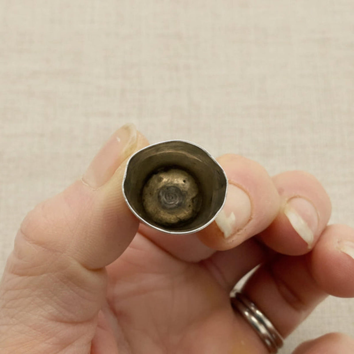 Hand holding a silver thimble showing the inside against a beige background