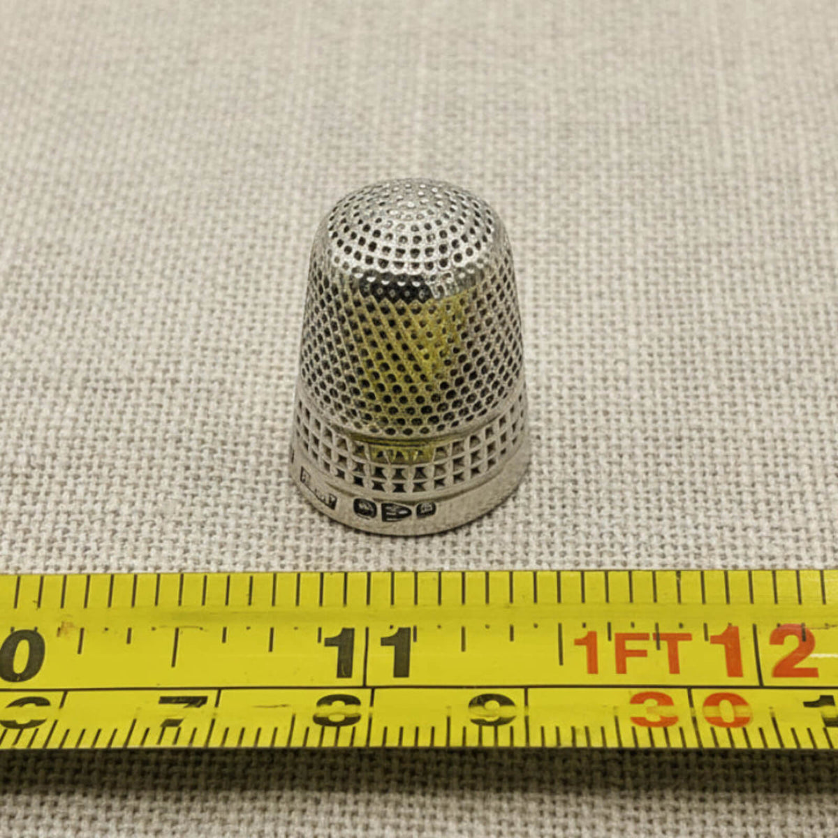 Silver thimble on a textured fabric background with a measuring tape for scale.