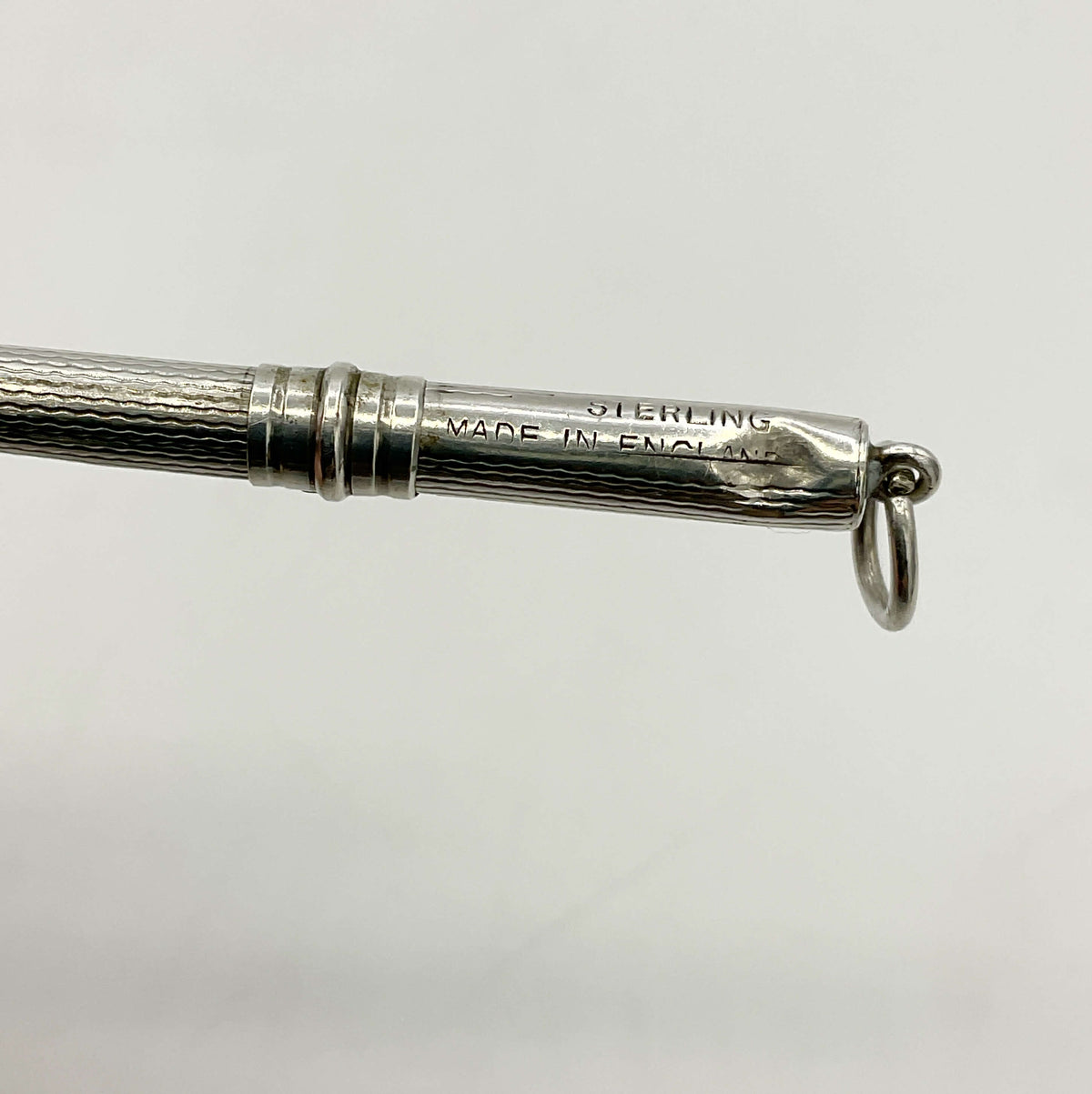Close-up of a Art Deco Sterling Silver Cocktail Whisk engraved 'STERLING MADE IN ENGLAND', and a small hanging ring on a plain light gray background.