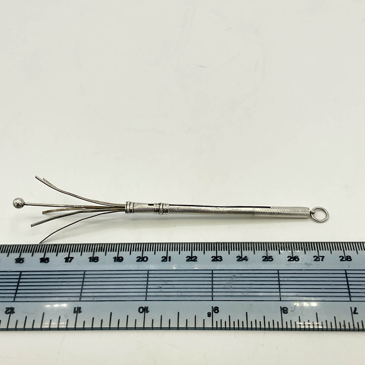 A Art Deco Sterling Silver Cocktail Whisk with multiple prongs and a small loop at the end, shown above a ruler for scale on a white background.