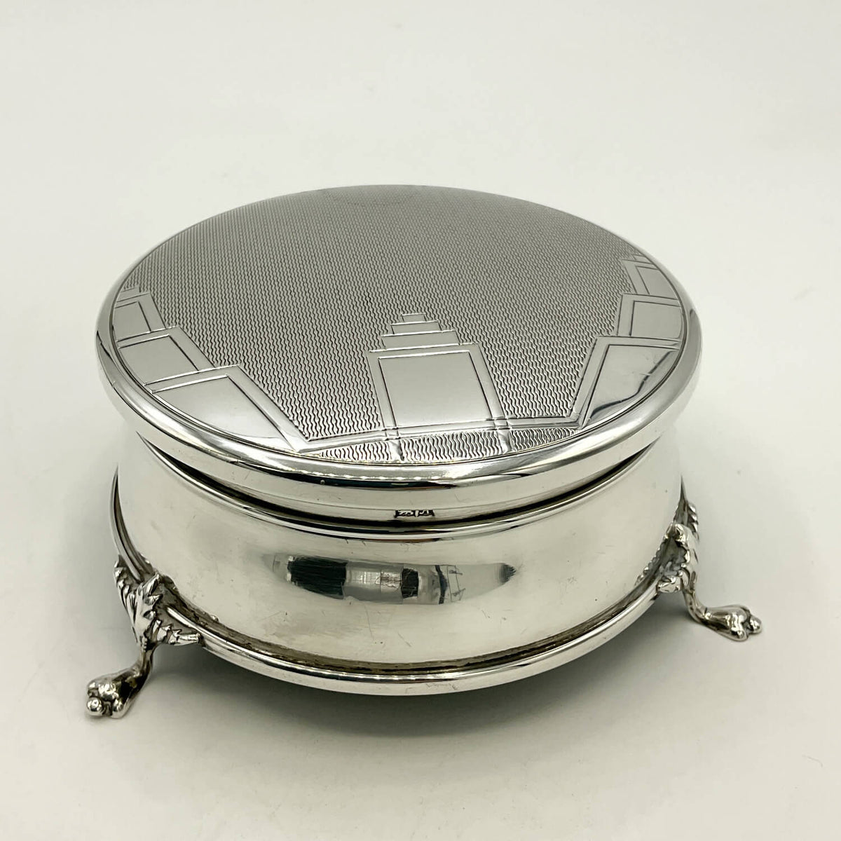 A vintage sterling silver lidded box with ornate claw feet and a textured pattern on the lid, photographed on a clean white background.