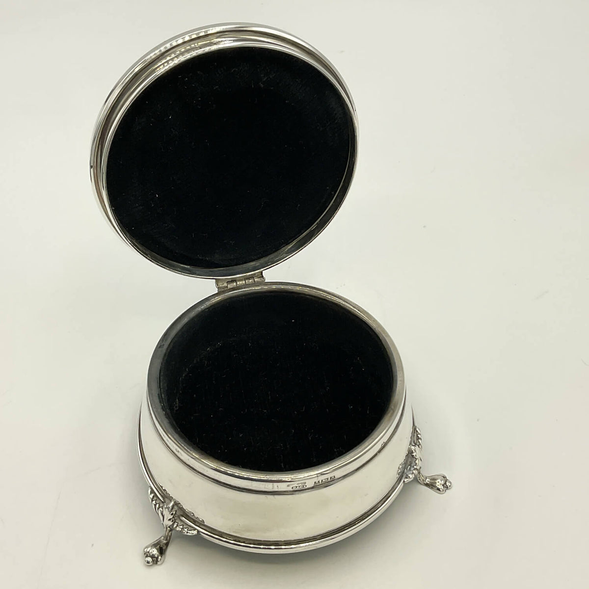 An open silver round jewelry box with a black velvet-lined interior, shown on a plain white background.