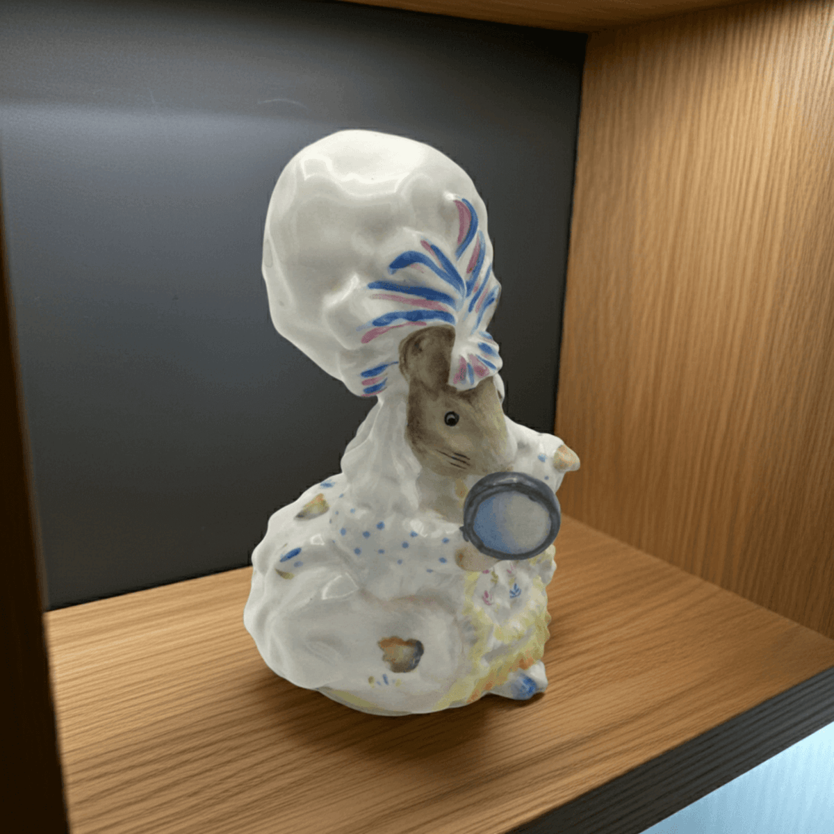 Decorative figurine of a mouse with a colorful hat on a wooden shelf.