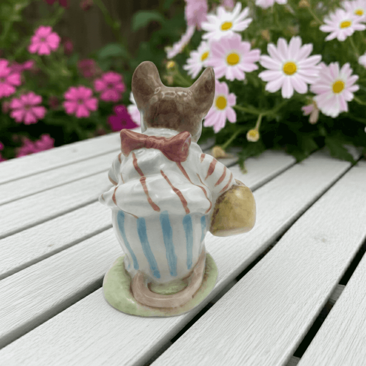 Small figurine of Mrs Tittlemouse on a wooden surface with flowers in the background