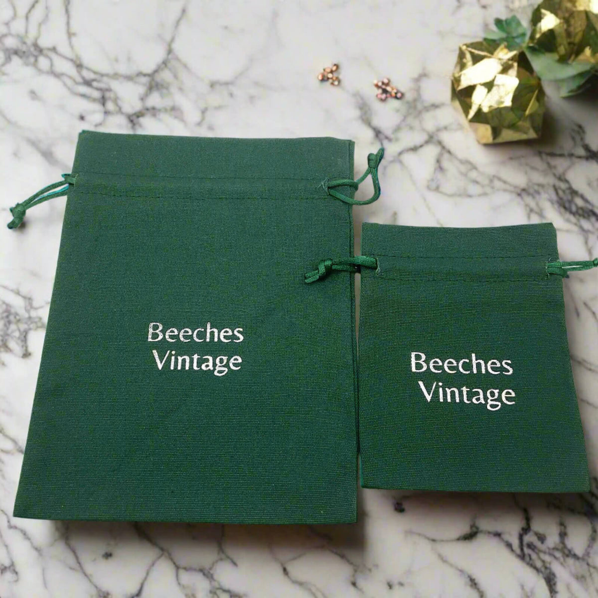 Two green 'Beeches Vintage' bags on a marble surface with golden decor items.