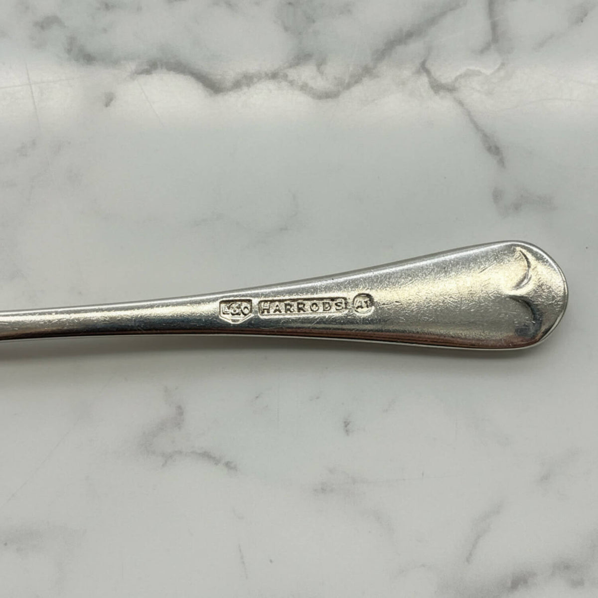 Silver coffee spoon with Harrods branding on a marble surface