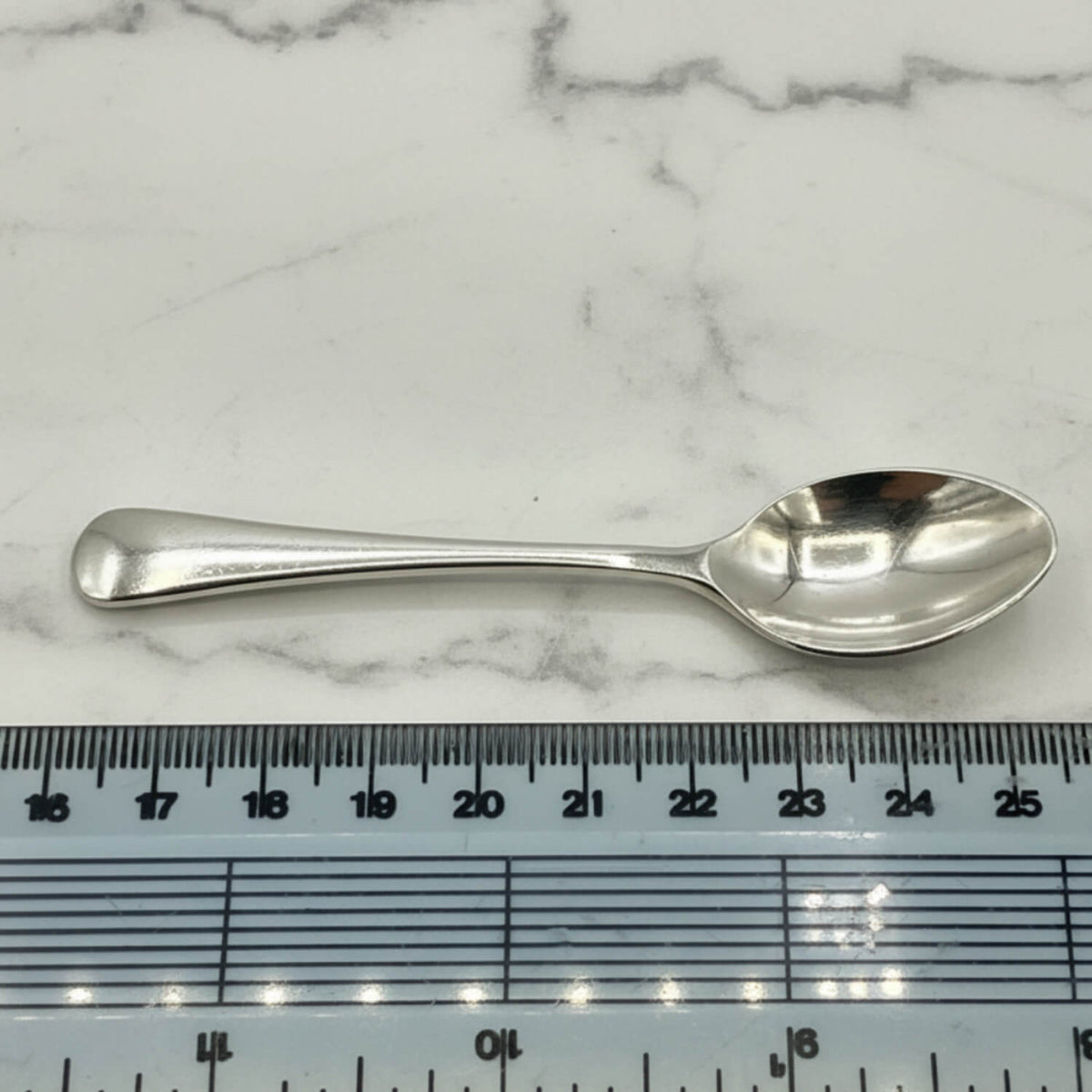 Silver coffee spoon on a marble surface with a ruler for scale