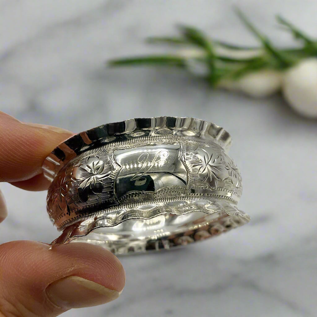 Silver napkin ring with floral patterns held by a hand on a marble background