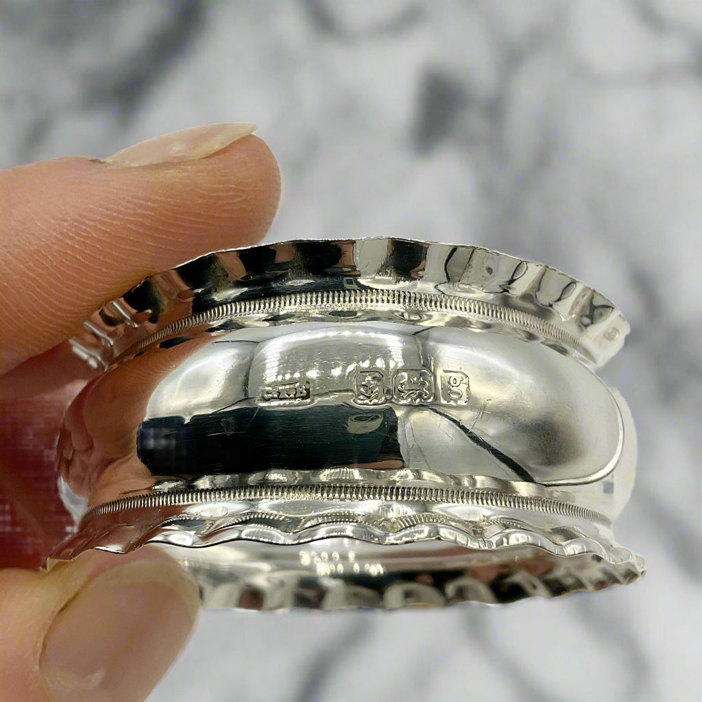 Silver decorative napkin ring held by a hand on a marble background