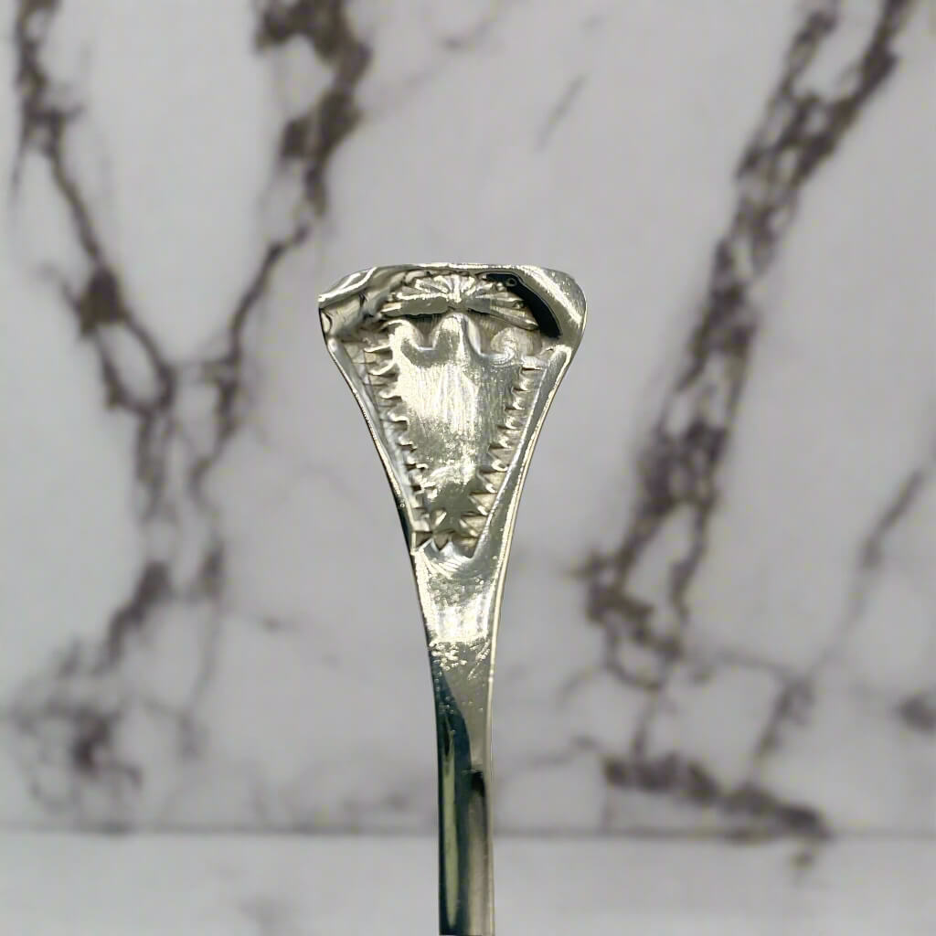Silver spoon handle with intricate design on a marble background