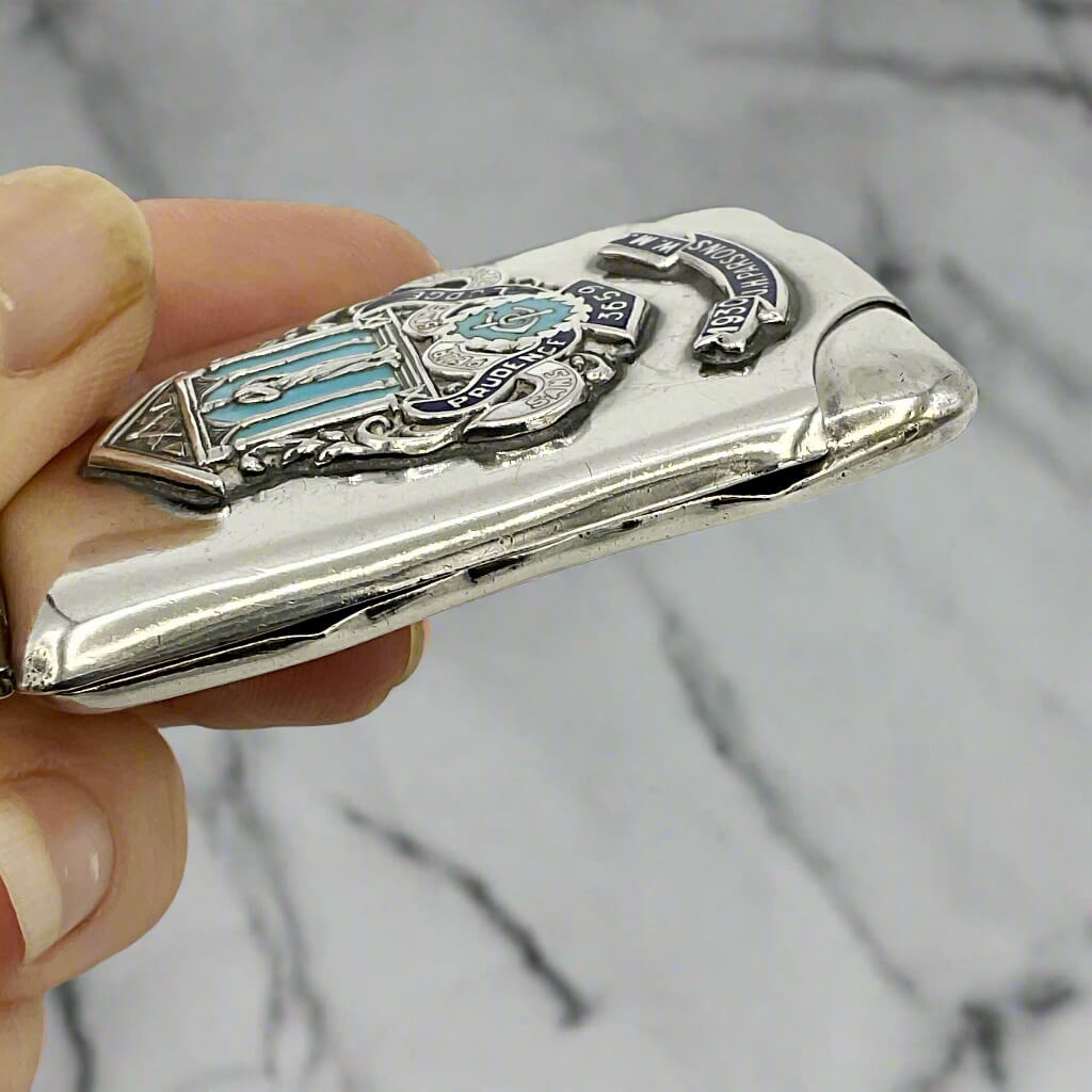Silver matchbook with Masonic emblem held by a hand against a marble background