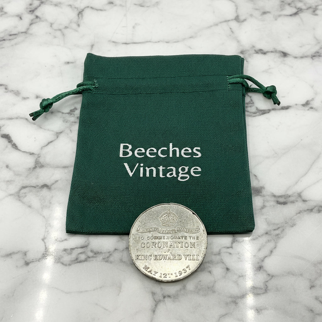 Silver coin with engraved text on a green drawstring bag with 'Beeches Vintage' branding on marble background 