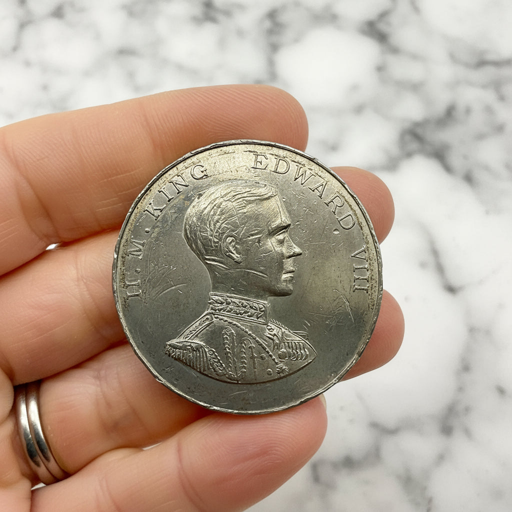 Silver coin with a portrait and text held between fingers against a white background