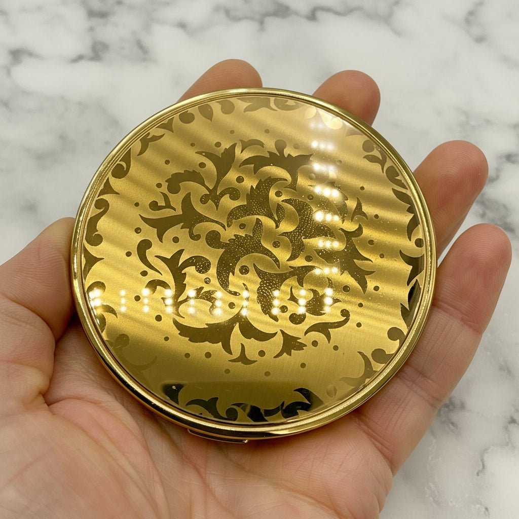 Gold decorative compact mirror held in a hand against a marble surface