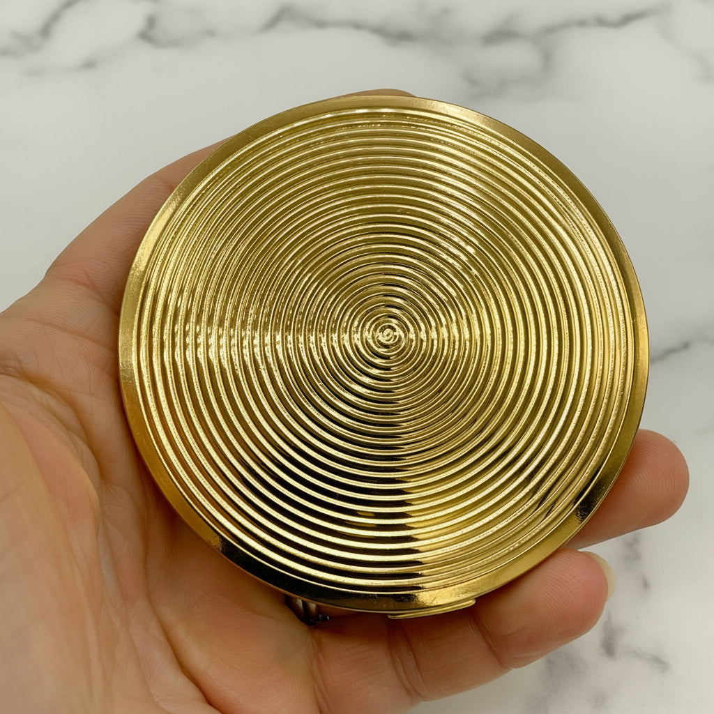 Gold compact powder case held in a hand against a neutral background