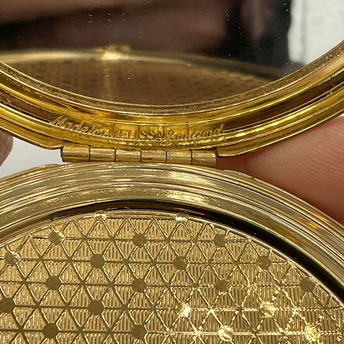 Close-up of a gold compact mirror with intricate design with Melissa and Made In England engraved 