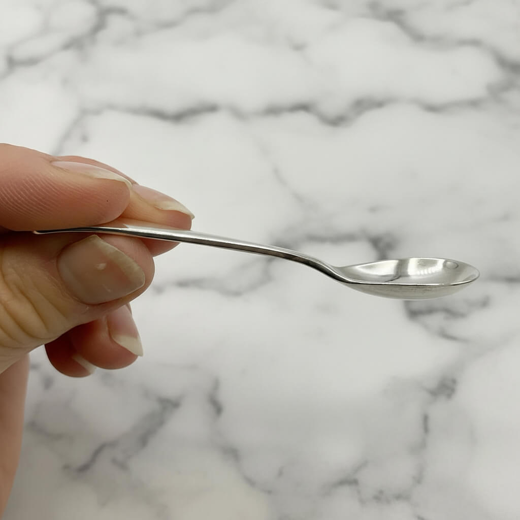 Hand holding a silver spoon against a marble background