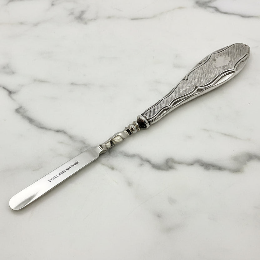 Silver cuticle pusher with decorative handle on a marble surface