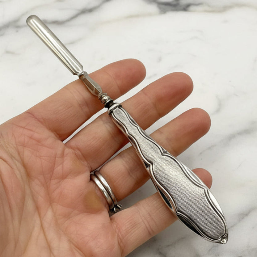 Silver cuticle pusher held in a hand with a marble background