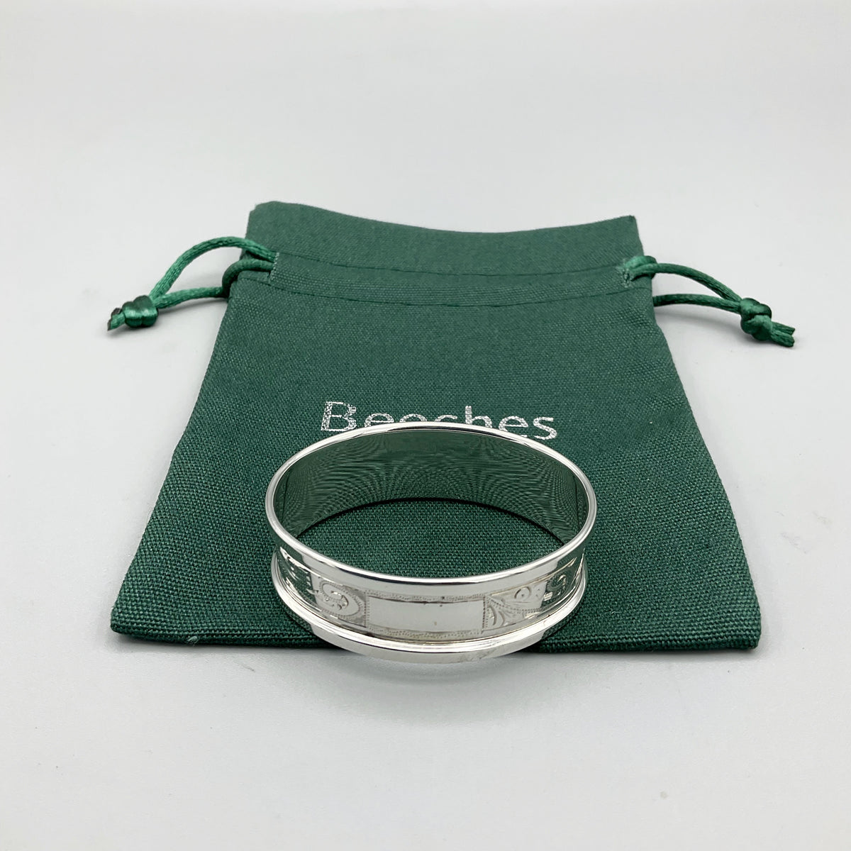 Engraved silver napkin ring sitting on a green cotton bag