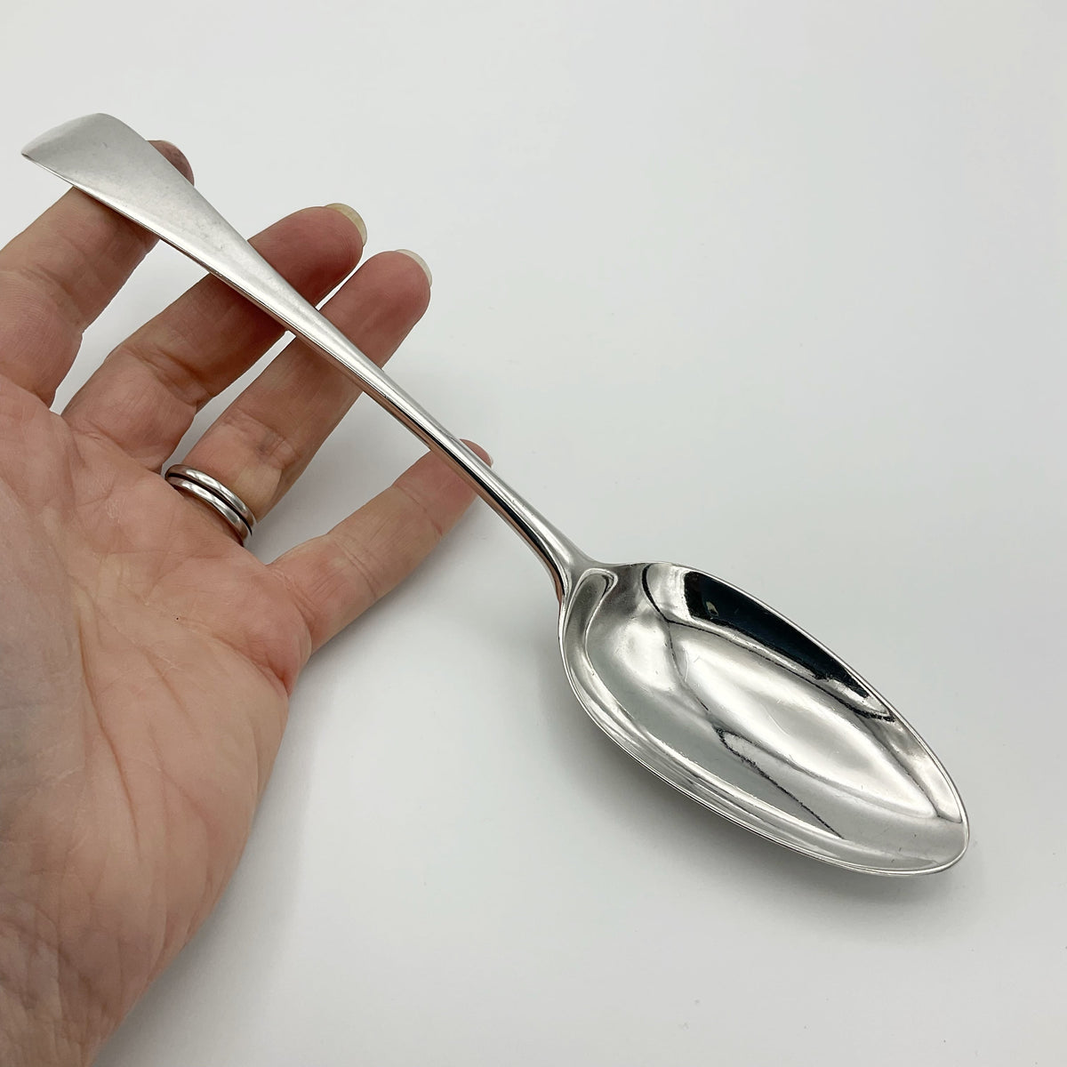 Antique Georgian 1788 silver serving spoon with ornate handle, displayed on a wooden surface, showcasing intricate vintage craftsmanship.