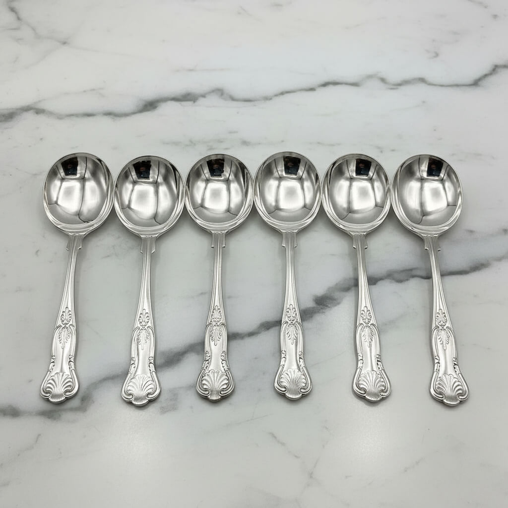 six silver plated soup spoons on a marble worktop