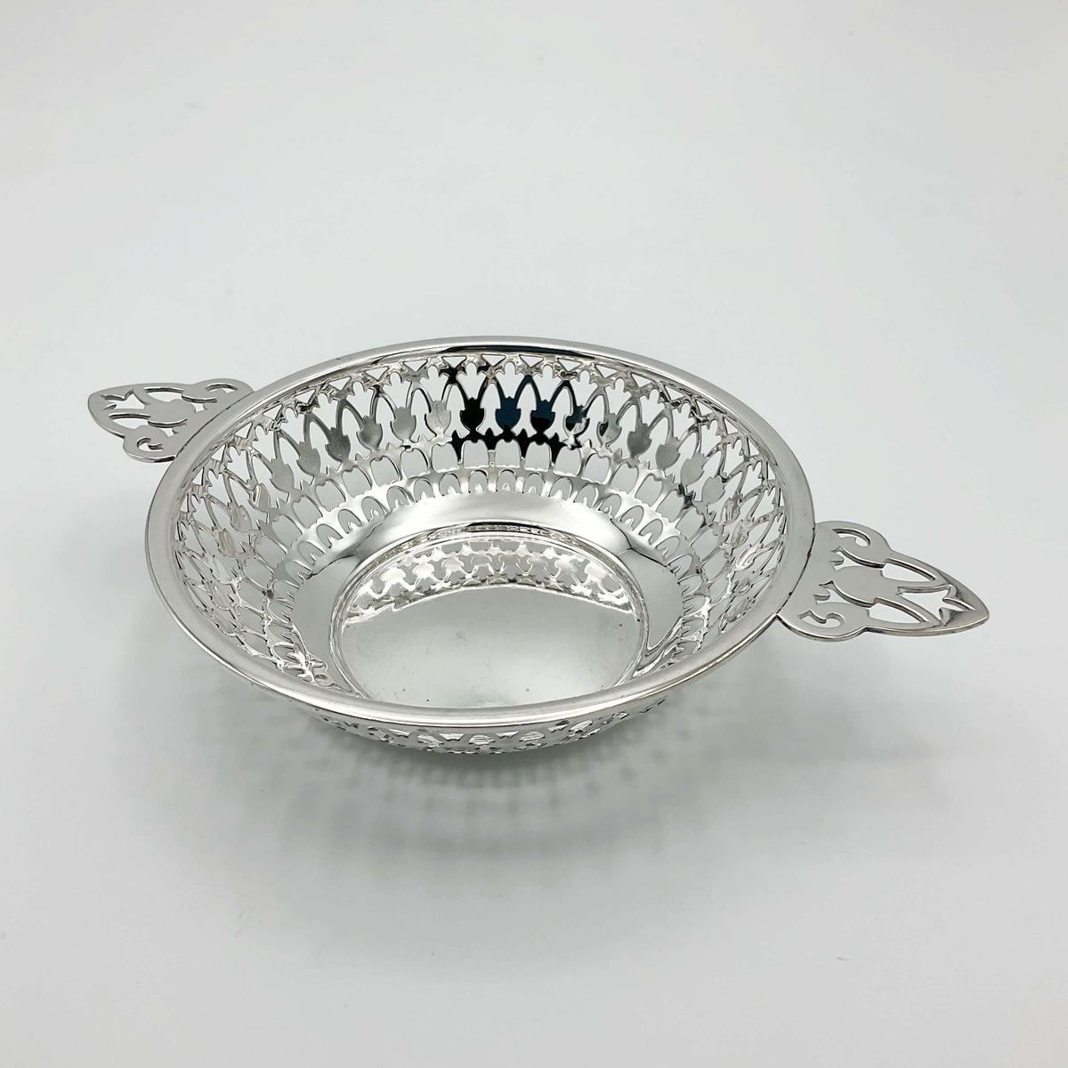Shiny silver pierced bowl with handles on white background 