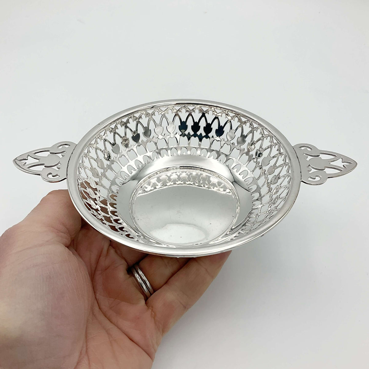 Shiny silver pierced bowl with handles sitting in a hand with a white background