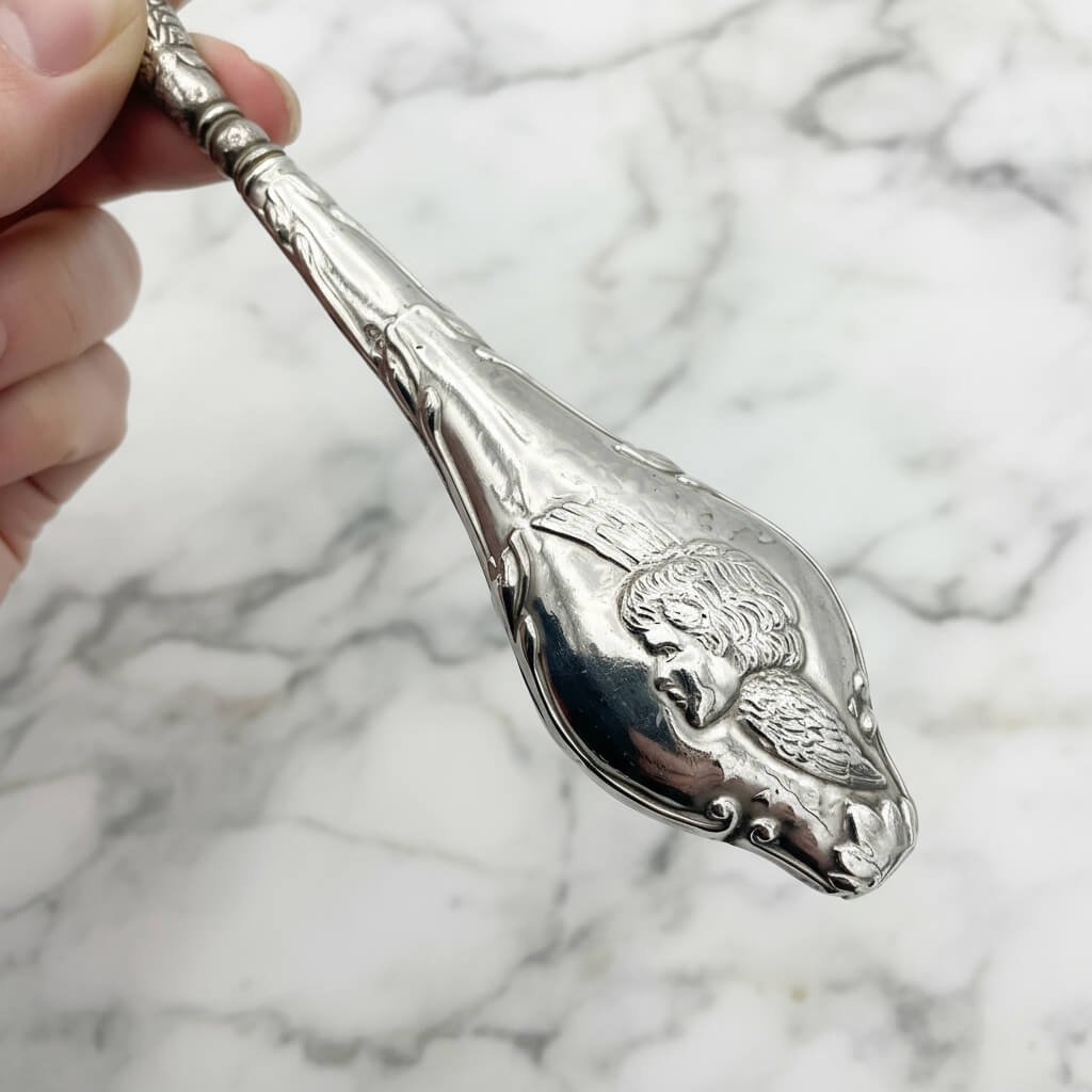 close up of a winged cherub on the silver handle of the button hook