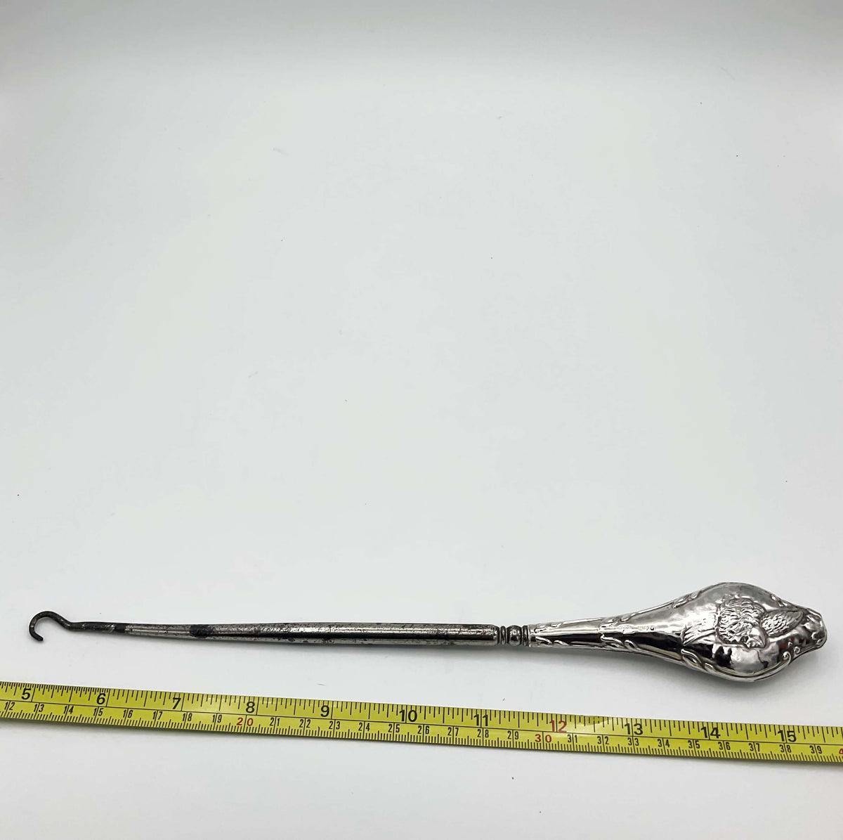 cherub on a button hook next to a tape measure for scale