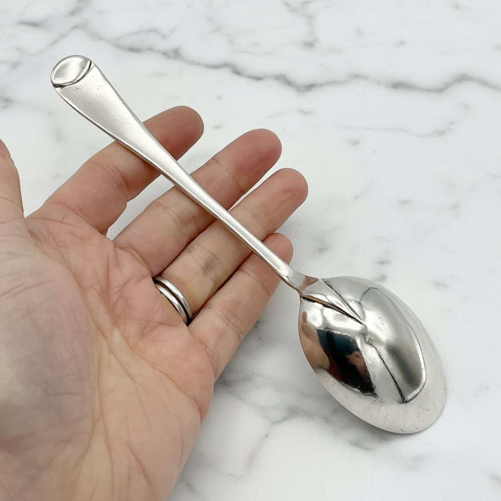 Back of Antique Silver Plated Dessert Spoon held in a hand on a marble worktop
