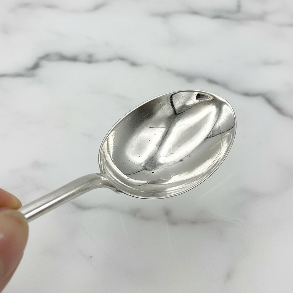 Bowl of silver plated dessert spoon held in fingertips with a marble surface