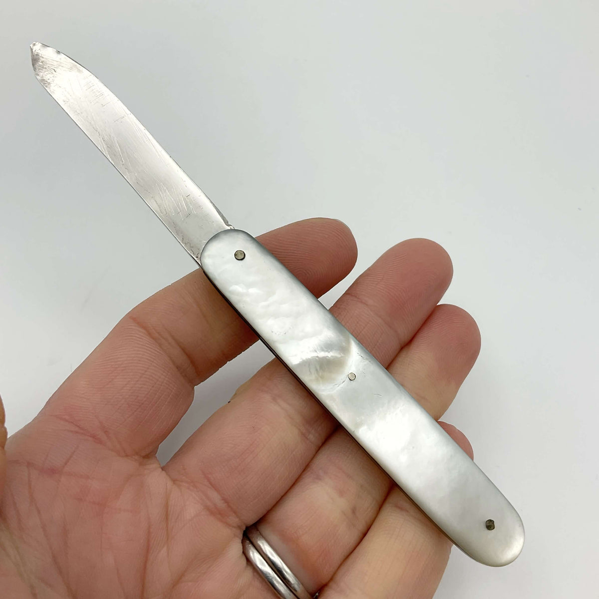Silver fruit knife with a mother of pearl handle held in a hand