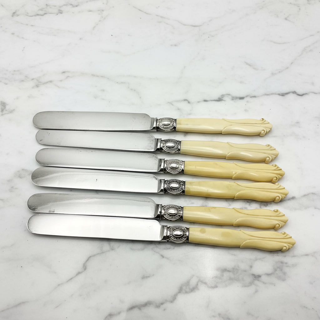 row of six silver plated bladed dessert knives with bone handles on a marble background