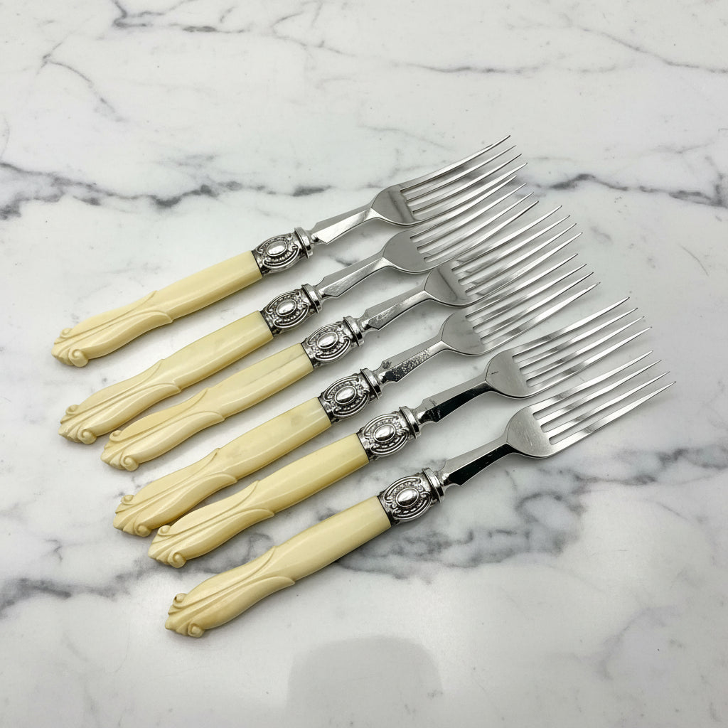 row of six dessert forks with bone handles on a marble background