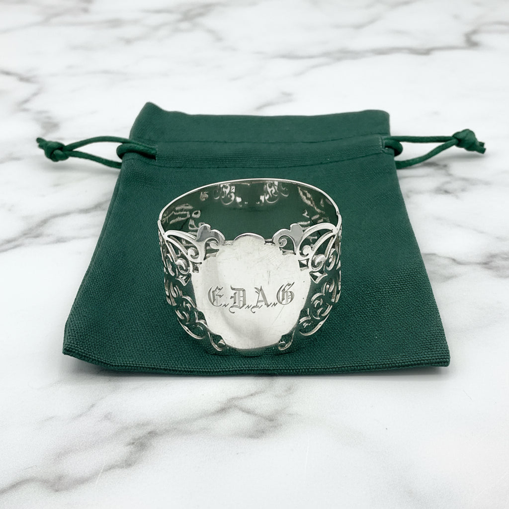 Shiny napkin ring with elaborate sides and EDAG in the centre, sitting on a green cotton bag that has Beeches Vintage on it.