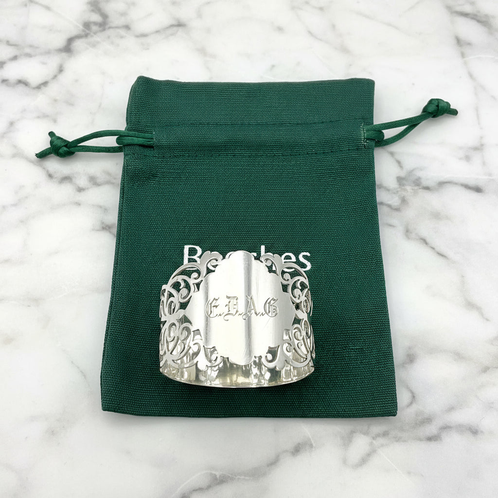 Shiny napkin ring with elaborate sides and EDAG in the centre, sitting on a green cotton bag that has Beeches Vintage on it.