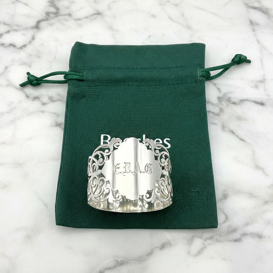 Shiny napkin ring with elaborate sides and EDAG in the centre, sitting on a green cotton bag that has Beeches Vintage on it.